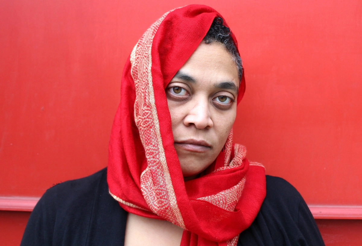 Donna-Michelle St. Bernard wearing a red scarf and black top in front of a red wall