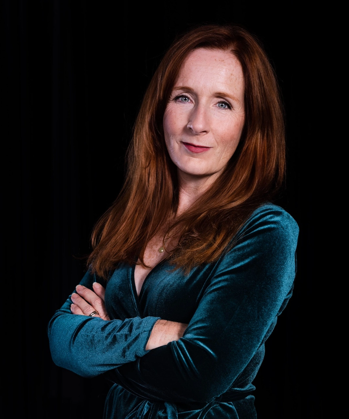 Mary Francis Moore in front of a dark background with red hair wearing a green dress